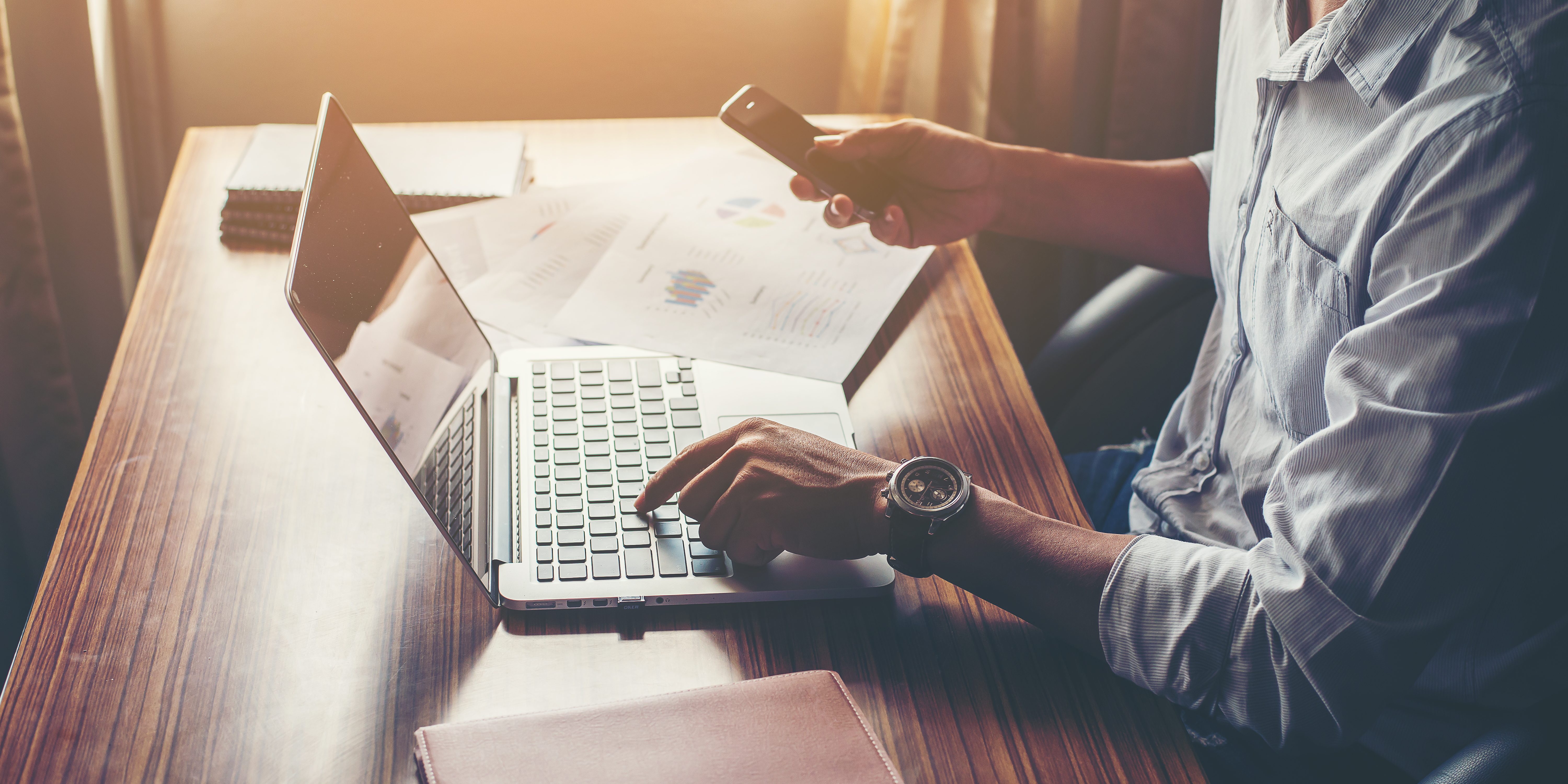 Businessman hands using cell phone with laptop at office desk.